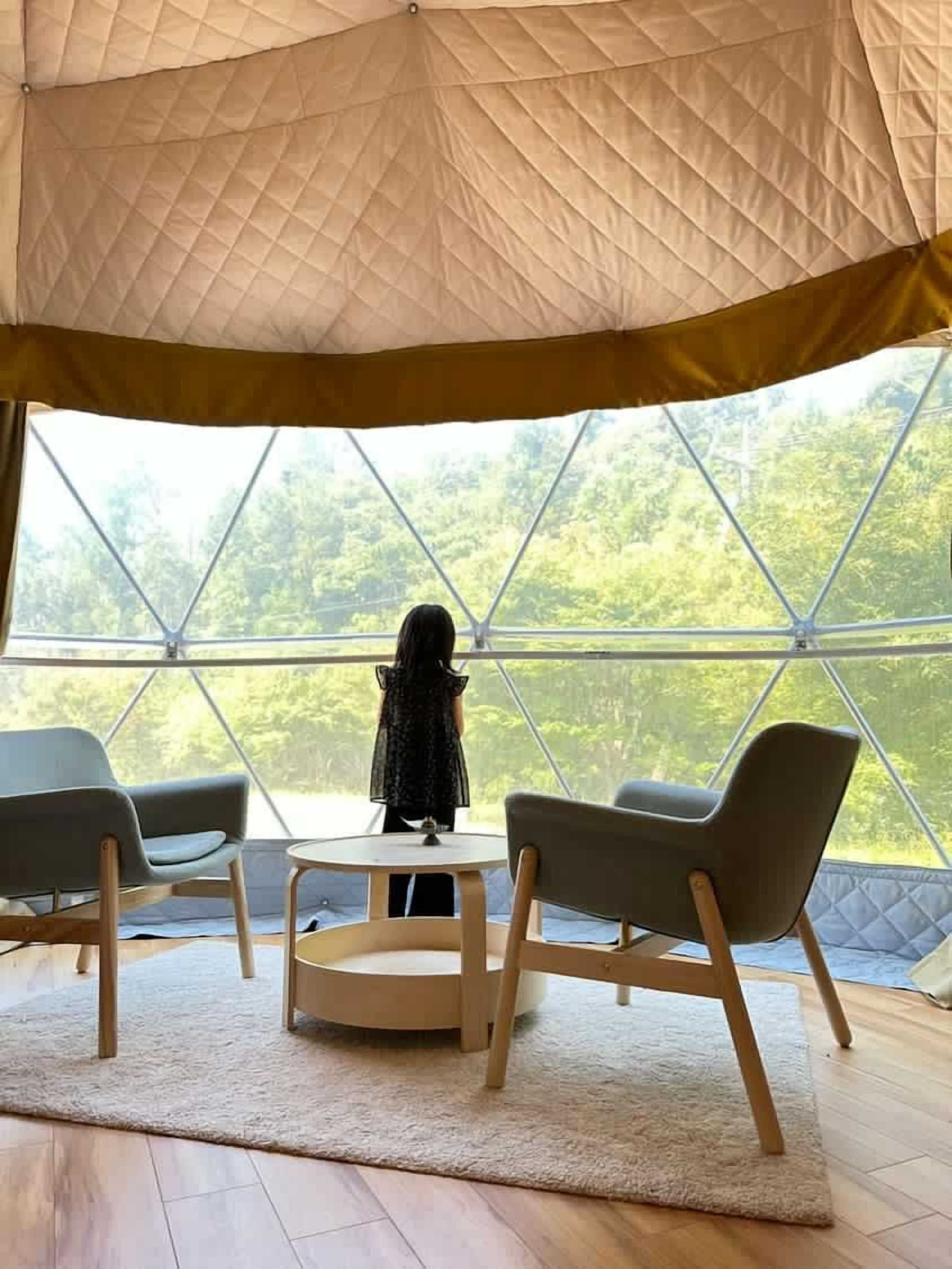 Una habitación con carpa, una mesa redonda y dos sillas, ventanas amplias que dan a zonas verdes.