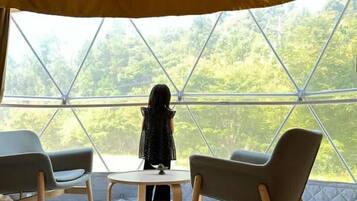 Una habitación con carpa, una mesa redonda y dos sillas, ventanas amplias que dan a zonas verdes.