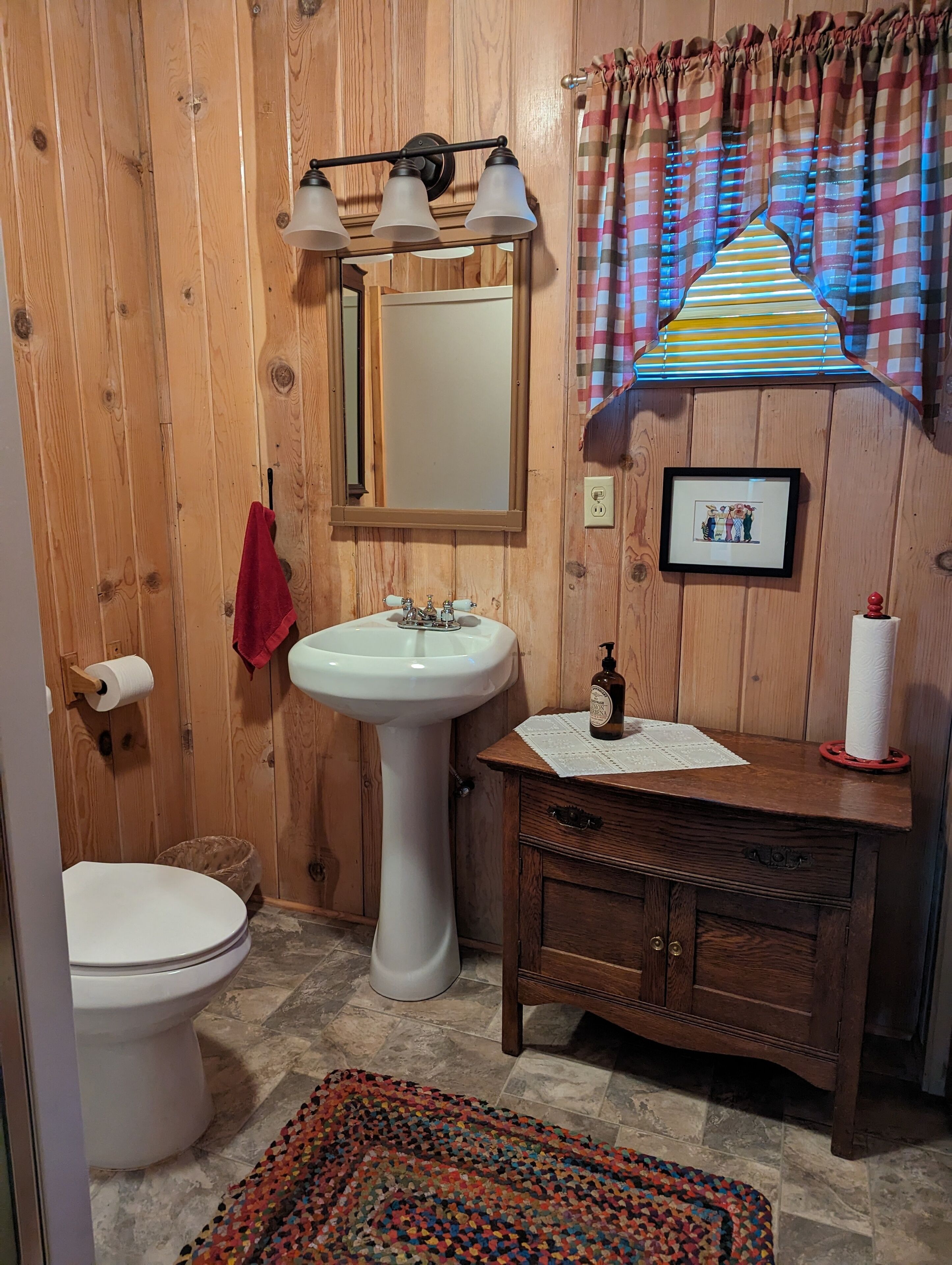 Une salle de bain en bois avec un lavabo sur pied blanc, un miroir, un meuble-lavabo en bois et des toilettes.