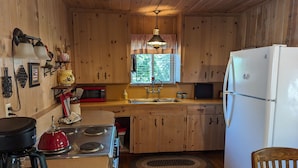 Une cuisine rustique, située dans une cabane en bois, équipée d’une cuisinière, d’un four à micro-ondes, d’un évier et d’un réfrigérateur.