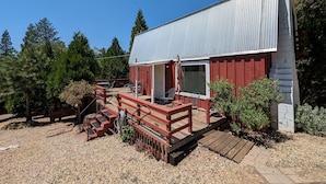 Un petit bâtiment d’un seul étage, à l’extérieur rouge et doté d’un toit en métal, comprenant une terrasse avec des sièges extérieurs et un escalier menant à l’entrée.