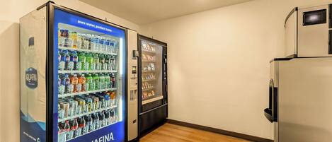Una habitación con piso de madera, un refrigerador y dos máquinas expendedoras que dicen 'AQUAFINA'.