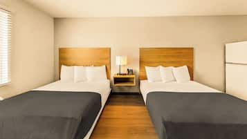 Una camera d'albergo con due letti, un comodino con una lampada e una testiera in legno.