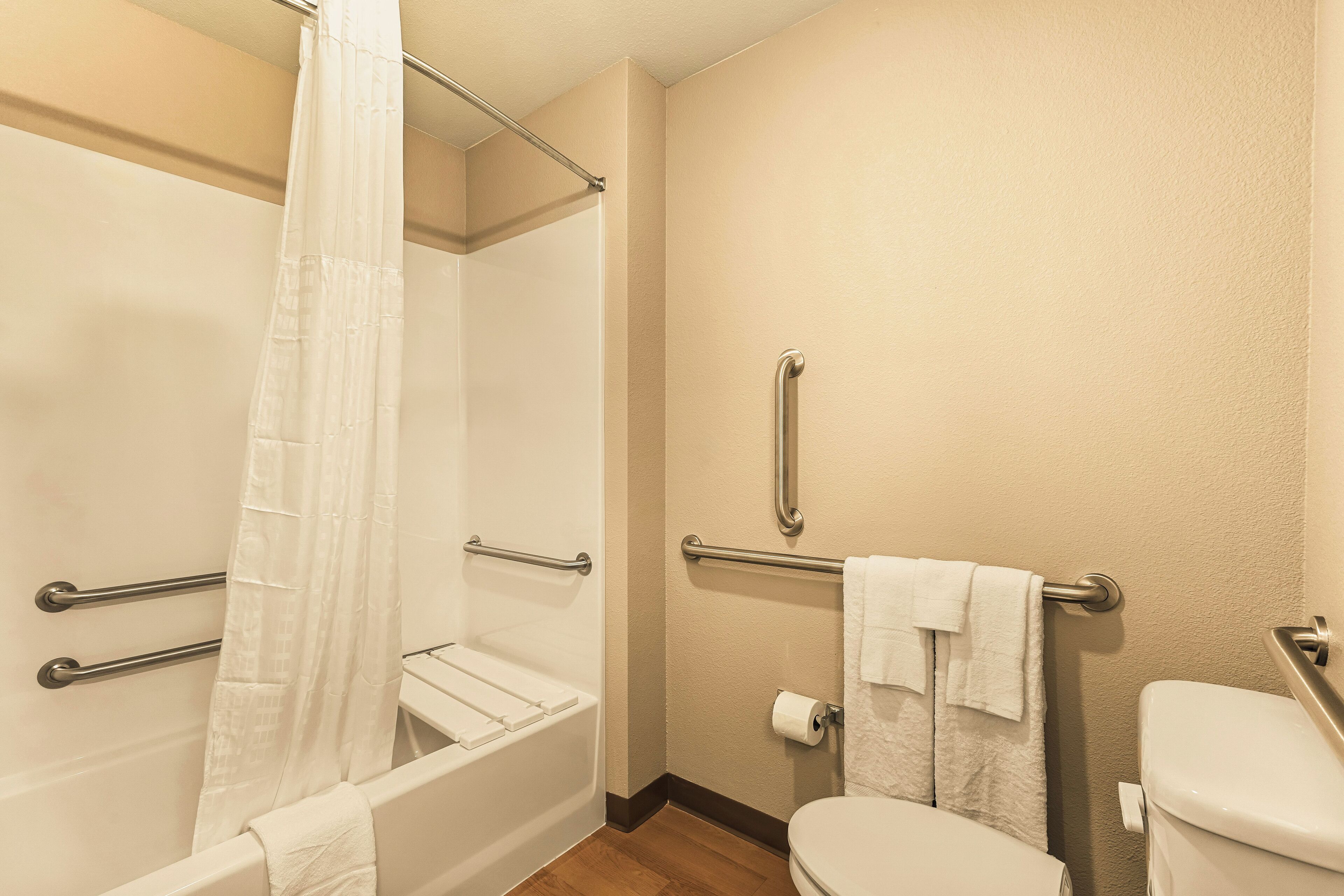 A bathroom with a shower, toilet, and grab bars.