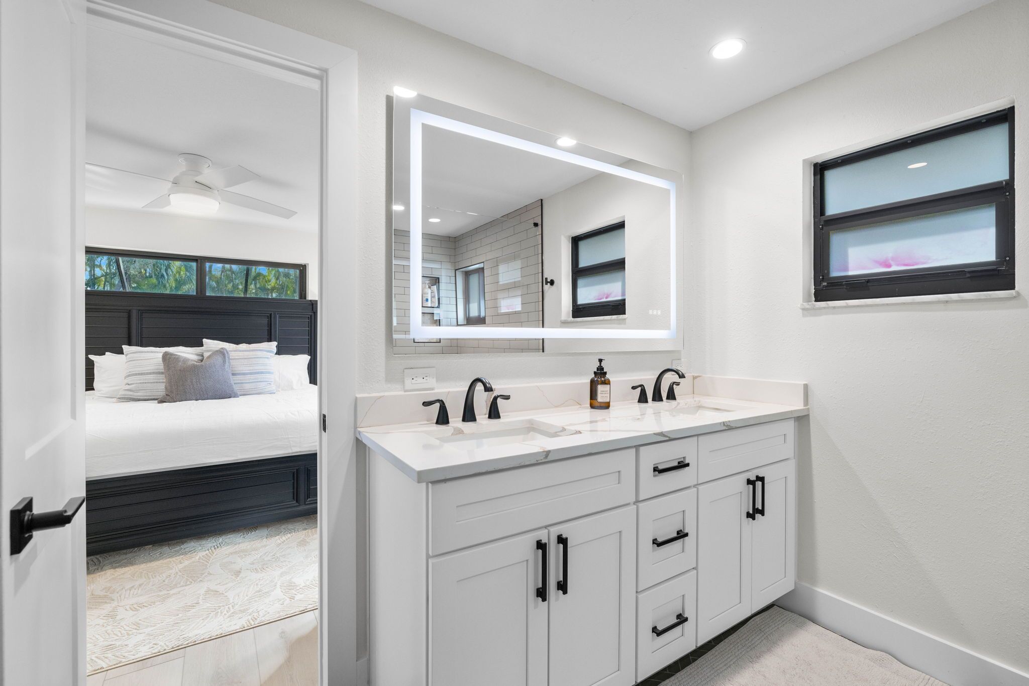 A modern bathroom with a large mirror, white cabinetry, and a double sink.