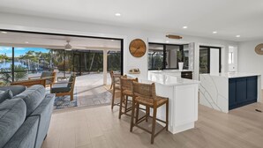 Cozinha moderna com ilha branca, banquetas de madeira e uma grande janela com vista para uma área de piscina.