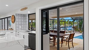 Cozinha moderna com ilha de mármore, área de refeições com vista para a piscina e uma placa indicando a cozinha.