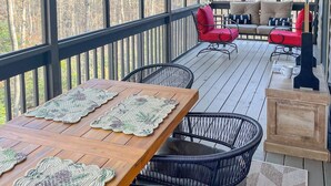 A covered outdoor deck with a wooden table, black wicker chairs, and red and beige sofas. - Cute 3-3 cabin with fire pit, games, resort amenities! (Ellijay)