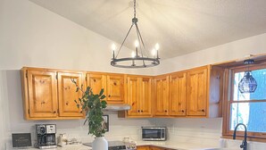 A modern kitchen with wooden cabinets, a central island, a coffee machine, a microwave, and a large window. - Cute 3-3 cabin with fire pit, games, resort amenities! (Ellijay)