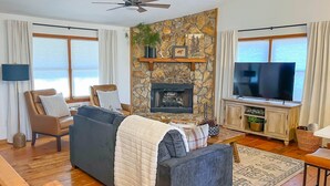 A living room with a stone fireplace, a sofa, a television, and a ceiling fan. - Cute 3-3 cabin with fire pit, games, resort amenities! (Ellijay)