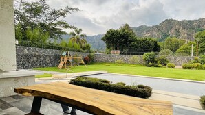 A wooden bench with a stone wall backdrop, a stone pathway, and a view of a mountain range. - Casa del Valle, cozy and with a beautiful view.  (Tepoztlán)