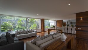 A modern living room with a sofa, a wooden coffee table, and a view of lush greenery outside. - Casa del Valle, cozy and with a beautiful view.  (Tepoztlán)