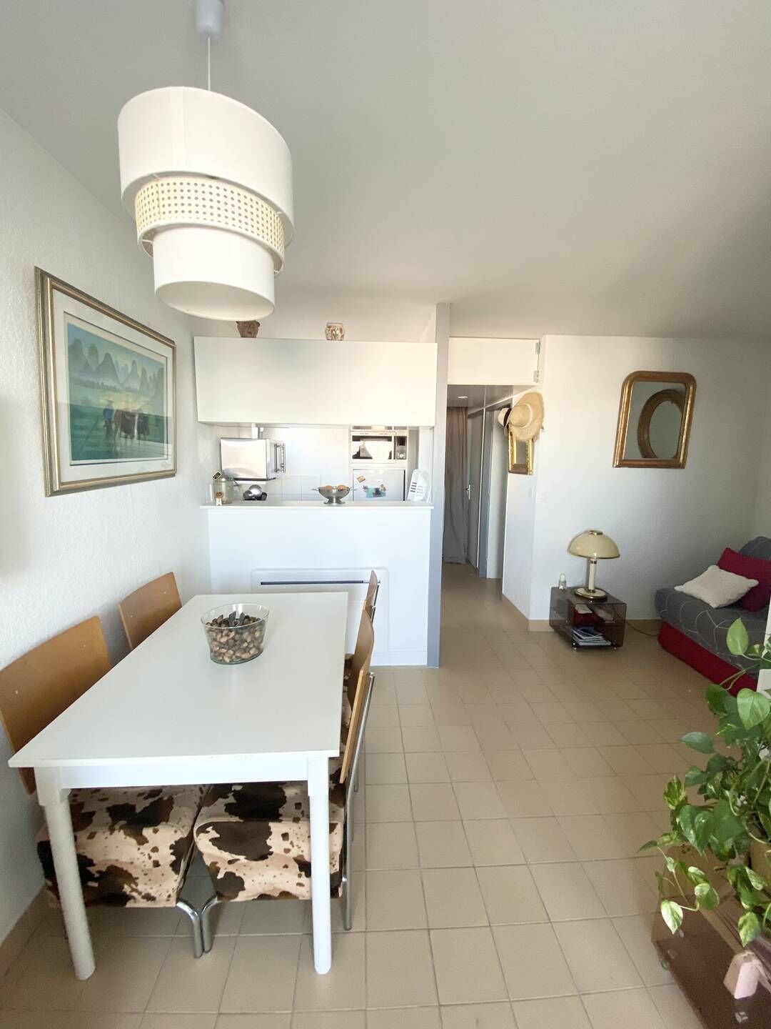 Una cocina moderna con armarios blancos, una mesa de comedor con una silla estampada de vaca, y una lámpara colgante.