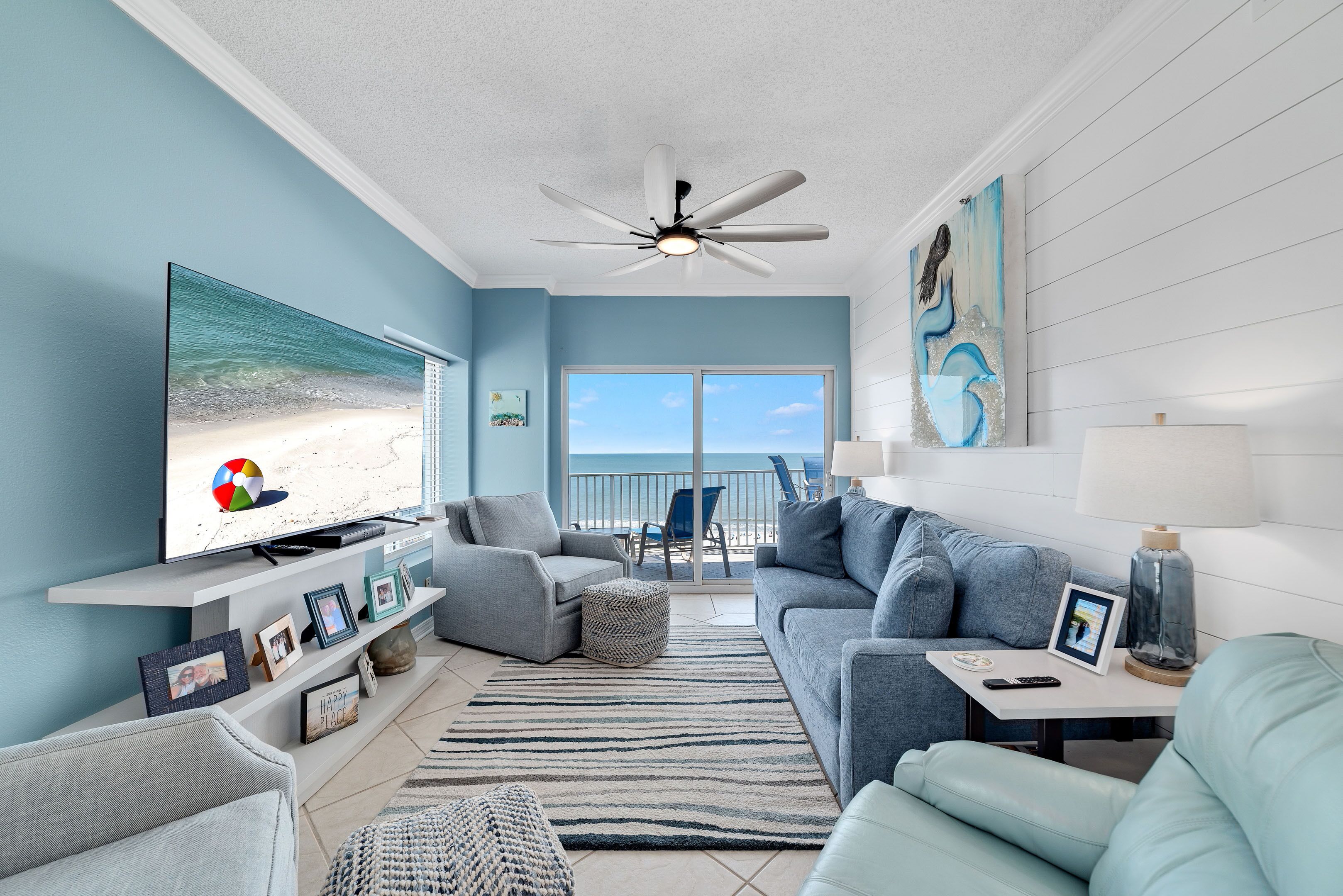 Ein Wohnzimmer mit Fernseher, Sofas, Deckenventilator und Blick auf den Strand.