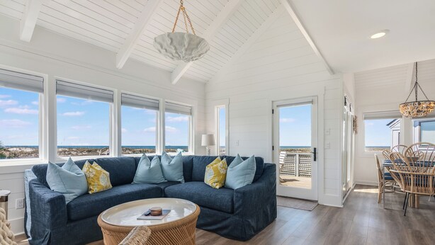 Een ruime woonkamer met een grote hoekbank, een ronde salontafel en een eethoek met rieten stoelen.