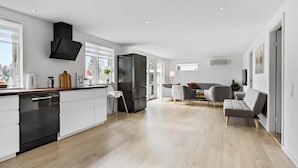 A modern kitchen with a built-in dishwasher and a dining area with a grey sofa and a small table. - Gorgeous home in Melby with WiFi (Melby)