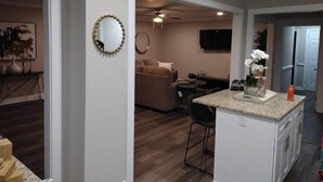 Eine moderne Küche mit Kochinsel, ein Essbereich mit Sofa und ein Wohnzimmer mit Fernseher.