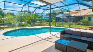 A covered outdoor swimming pool with a view of a house and greenery. - Indian River: Tranquil Waterfront Retreat (Cocoa)