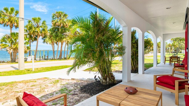 A covered outdoor seating area with a view of the beach and palm trees. - Indian River: Tranquil Waterfront Retreat (Cocoa)