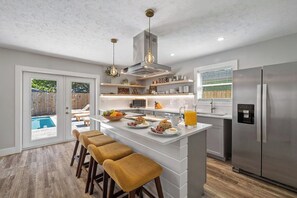 A modern kitchen with a central island, stainless steel appliances, and a pool visible through the sliding doors. - Bikes, Pool, Fire Pit, Bonfires • Near Pier Park & Beaches | G By The Sea (Panama City Beach)