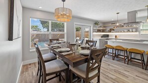 Una cocina moderna con armarios blancos, una isla central y un comedor con sillas de madera y una mesa para cuatro.