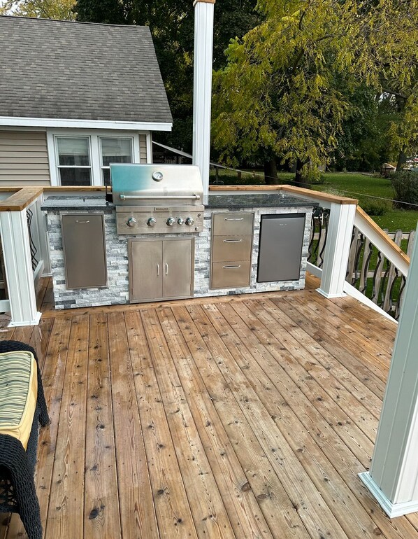 Una terraza exterior con una parrilla incorporada, detalles de piedra y piso de madera.
