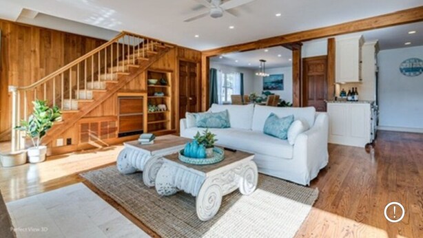 Ein geräumiges Wohnzimmer mit einem weißen Sofa, einer Holztreppe und einem Deckenventilator.