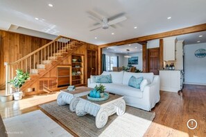 Un salón amplio con un sofá blanco, una escalera de madera y un ventilador de techo.