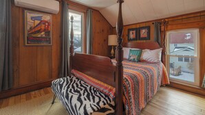 A bedroom with a wooden bed, a zebra-patterned chair, a window with a view of a snowy yard, and a poster of a train on the wall.