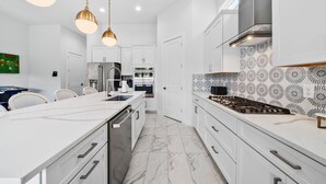 A modern kitchen with white cabinetry, a marble floor, and pendant lighting. - Liberty Luxor: Private Pool, Free Water Park, Golf View (Kissimmee)