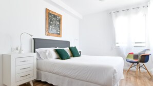 Une chambre bien rangée, avec un lit, une table de chevet, une chaise et une fenêtre avec des rideaux.