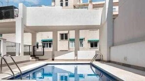 Une piscine accessible par des marches, entourée d’un bâtiment blanc doté de nombreuses fenêtres et de balcons.