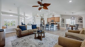 A spacious living room with a large ceiling fan, a dining area with a round table, and a kitchen in the background. - LAKEVIEW!, Heated Pool and Spa -Villa Lakeside Escape - Roelens Vacations (Cape Coral)