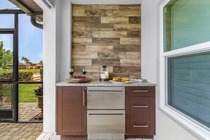 A kitchen with a stone backsplash, stainless steel appliances, and a window overlooking a garden. - LAKEVIEW!, Heated Pool and Spa -Villa Lakeside Escape - Roelens Vacations (Cape Coral)