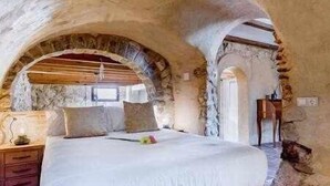 A bedroom with a stone archway, a bed, a nightstand, and a lamp. - Altea Suite Vault by Vero (Altea)