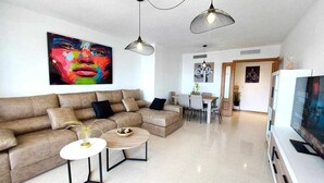 Ein modernes Wohnzimmer mit einem Ecksofa, zwei Couchtischen und Pendelleuchten.