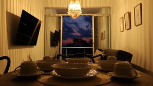 Un coin repas avec une table dressée pour quatre personnes, un luminaire suspendu et une vue sur le ciel par une fenêtre.