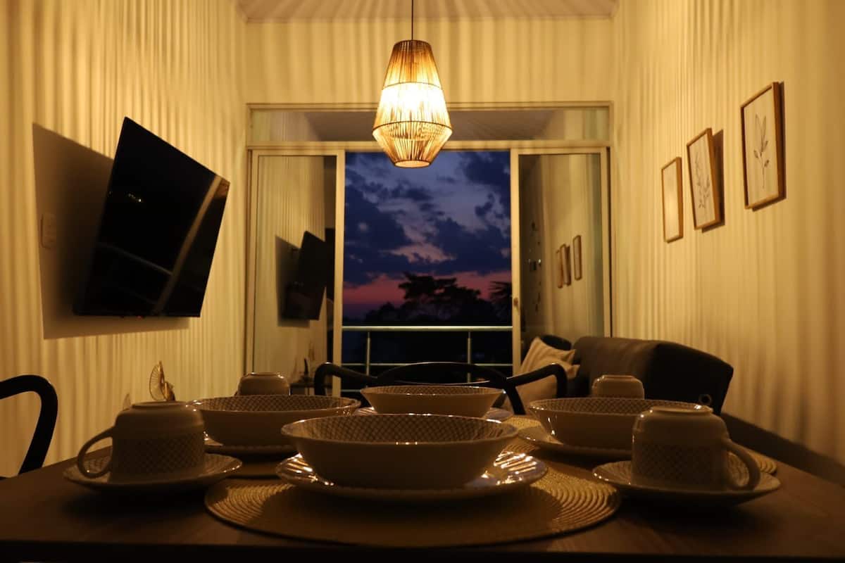 A dining area with a table set for four, a hanging light fixture, and a view of the sky through a window.