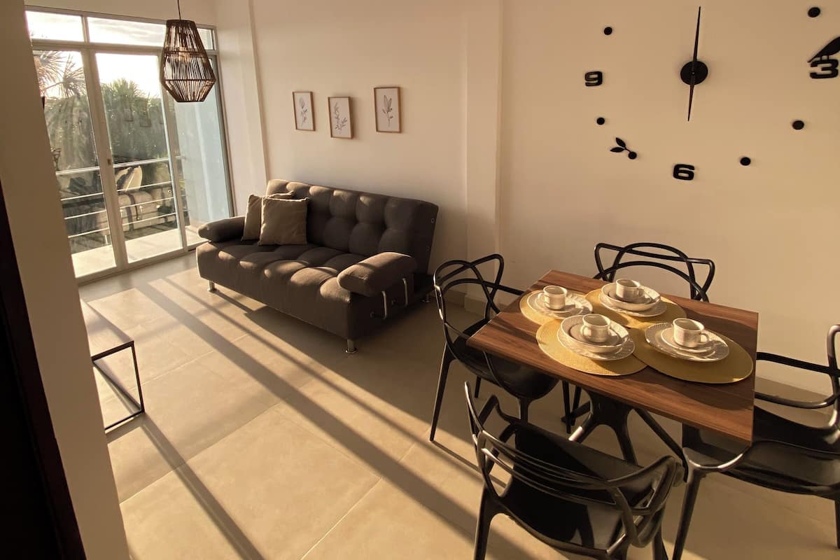 A modern living room with a sofa, dining table, chairs, and a large wall clock.