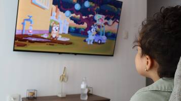 Una persona mirando televisión en una habitación con una mesa de madera, un ventilador y una botella.