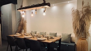Un espace repas avec une table en bois, des chaises noires et un luminaire suspendu.
