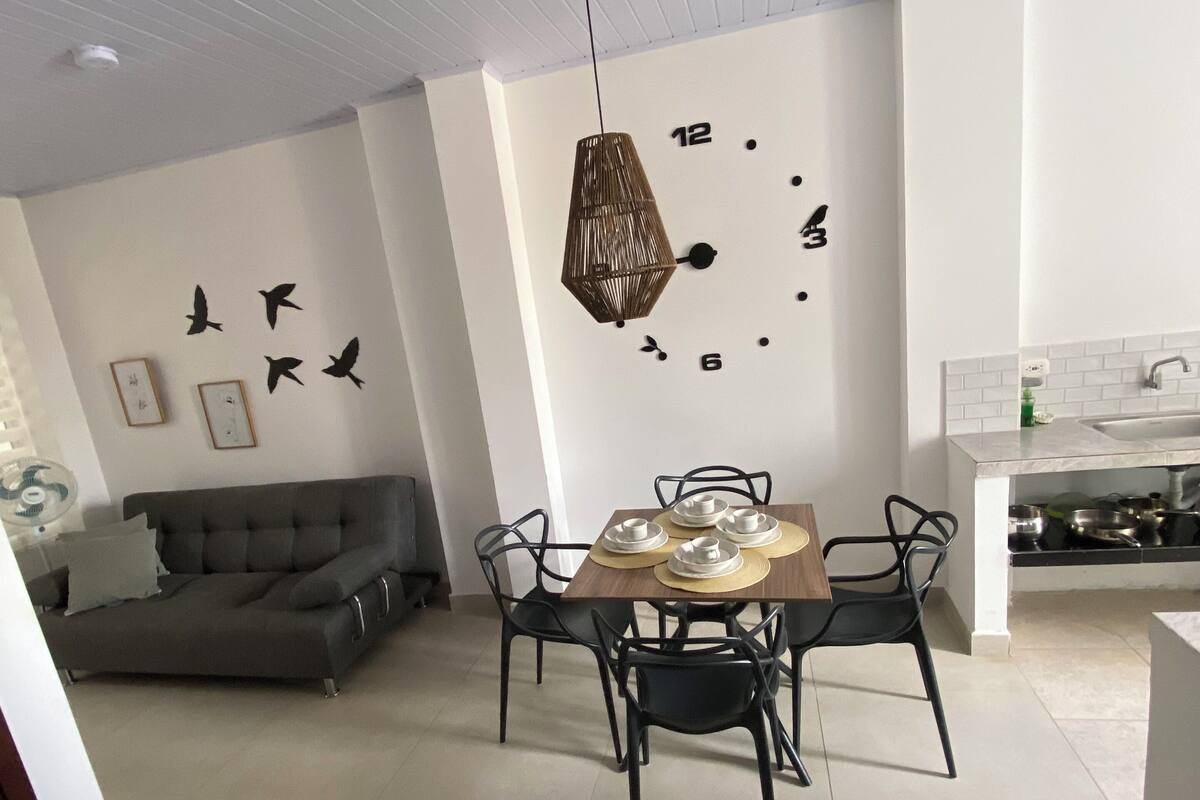 A modern living room with a dining area, featuring a sofa, chairs, a table, and a wall clock.
