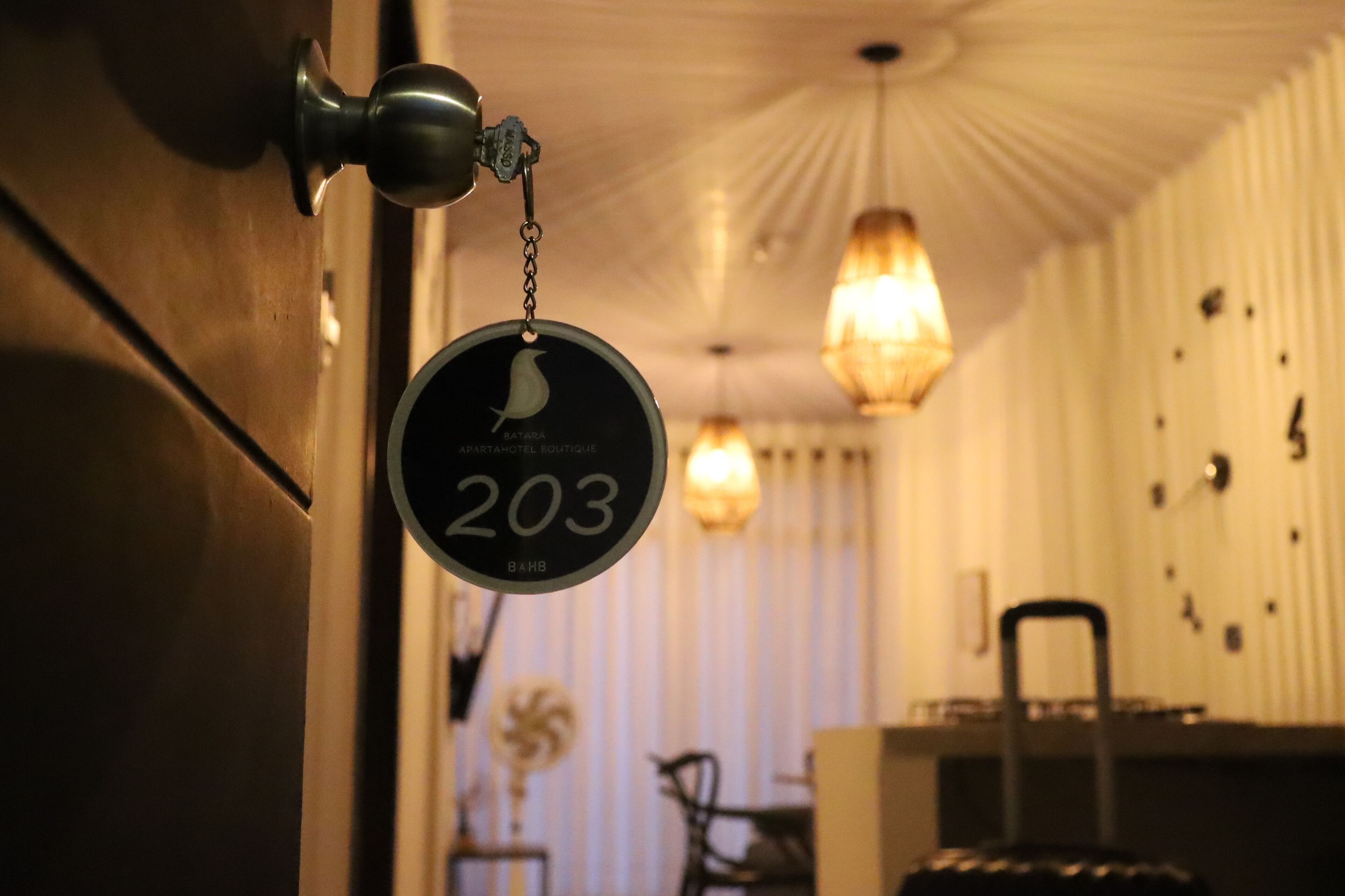 Une chambre d’hôtel avec une poignée de porte, une plaque numérotée « 203 » fixée au mur, et un lustre.