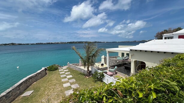 A coastal property with a stone wall, a palm tree, and a view of the sea.