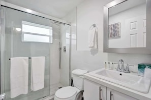 Ein modernes Badezimmer mit Duschkabine aus Glas, einem weißen Waschbecken und einem Spiegel darüber.
