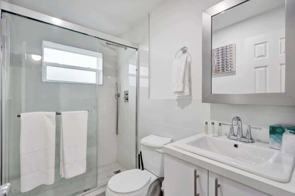A modern bathroom with a glass shower enclosure, a white toilet, and a sink with a mirror above it.