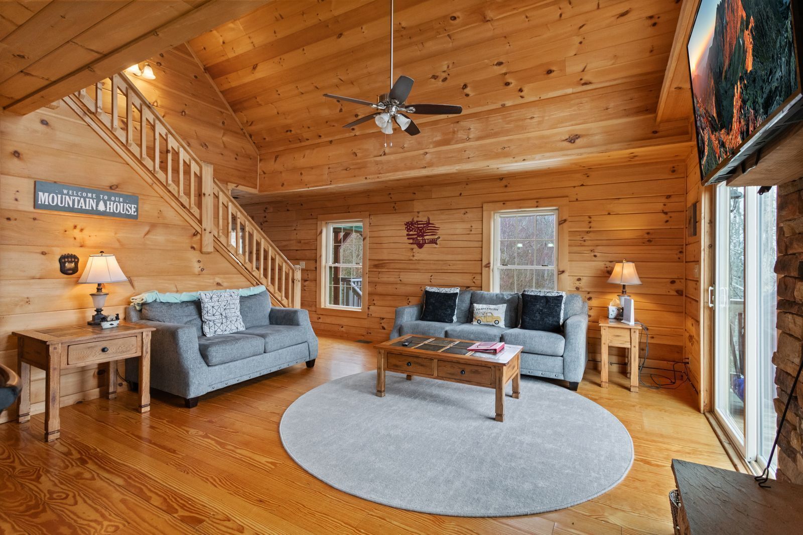 A cozy log cabin interior with two sofas, a coffee table, a wooden desk, and a staircase.