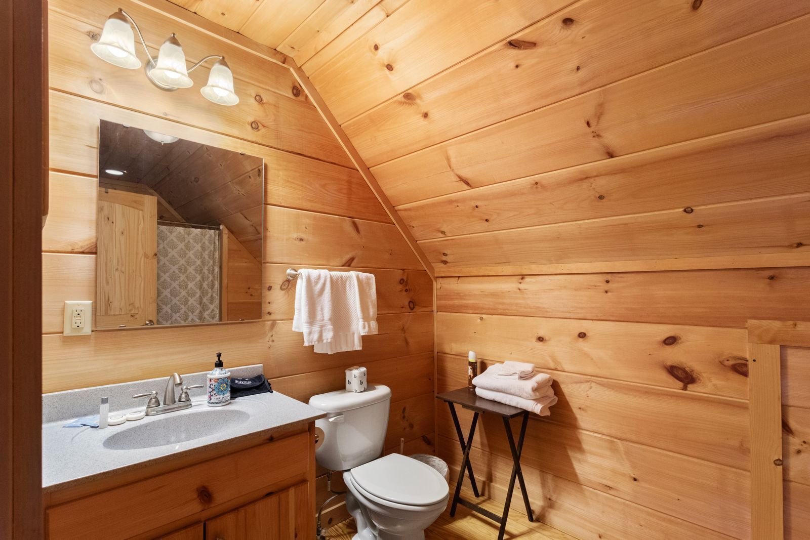 A wooden cabin bathroom with a sink, toilet, and a mirror.