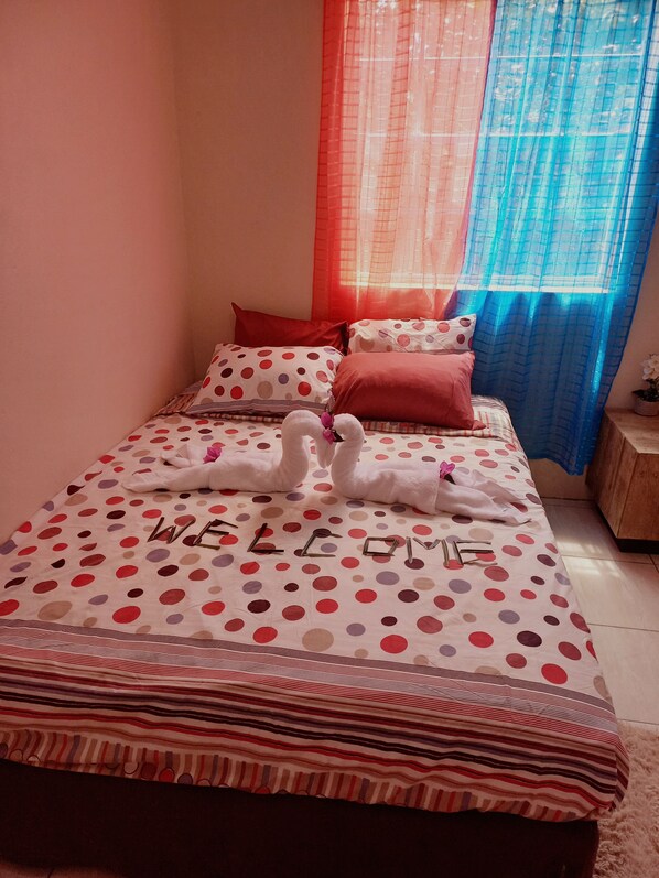 A bed with a polka dot and striped bedspread, two towels arranged as swans, and the word "WELCOME" spelled out on the bed.