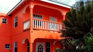 A two-story building with a red facade, a balcony with white balustrades, and a stone wall in front.